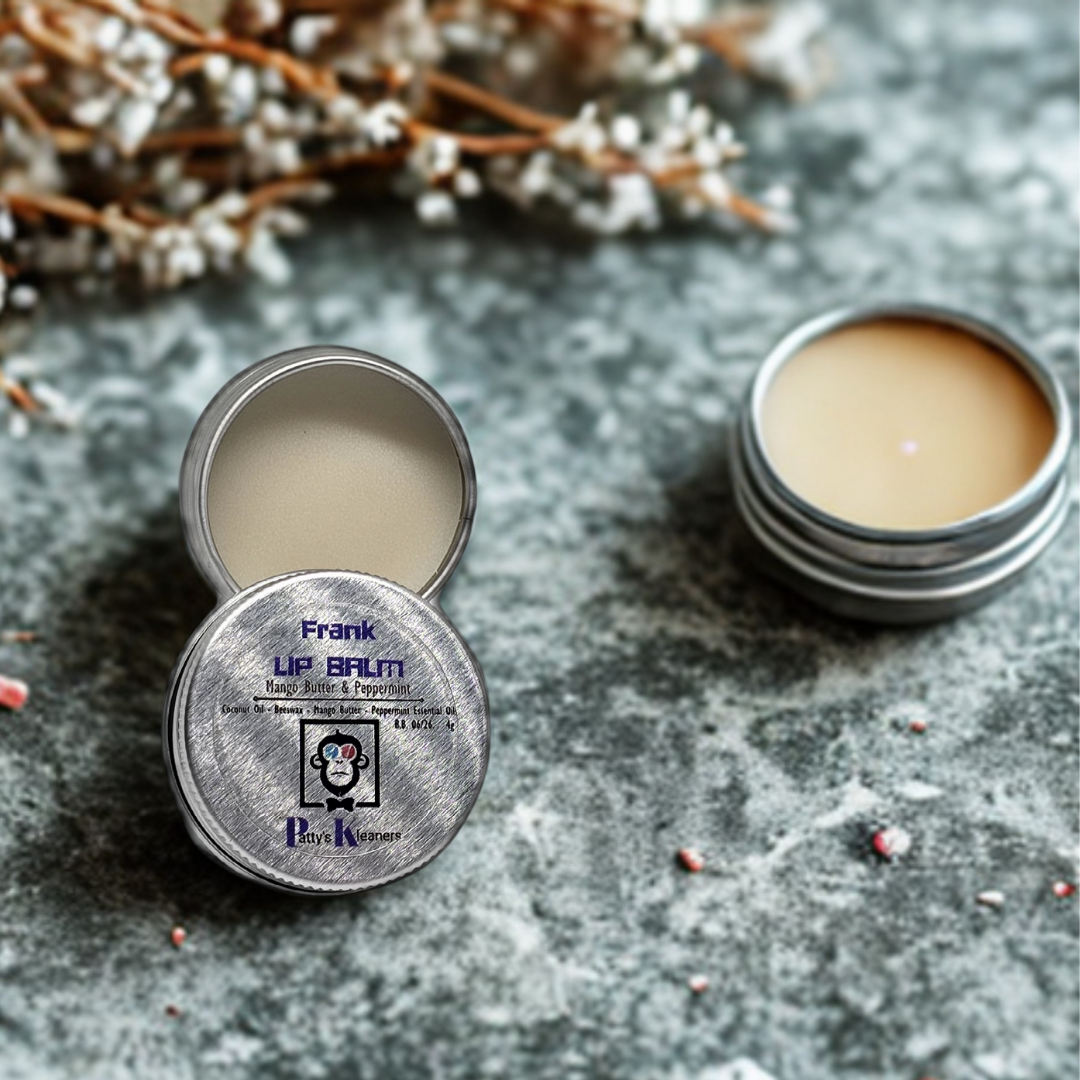Two tins of Frank Lip Balm on a textured surface with dried flowers in the background.
